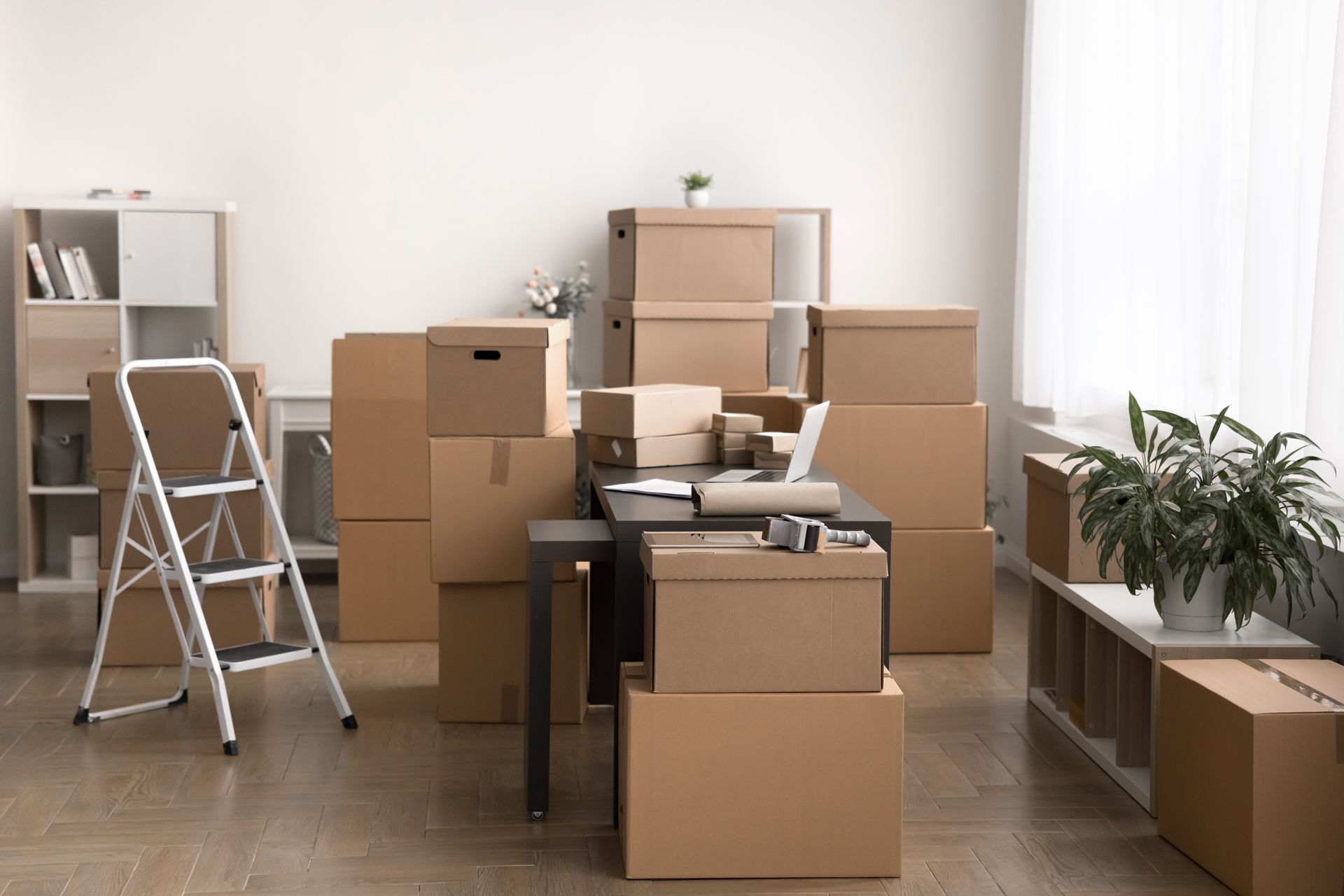 Two people seated at a white table, reviewing blueprints, with a laptop and tablet nearby