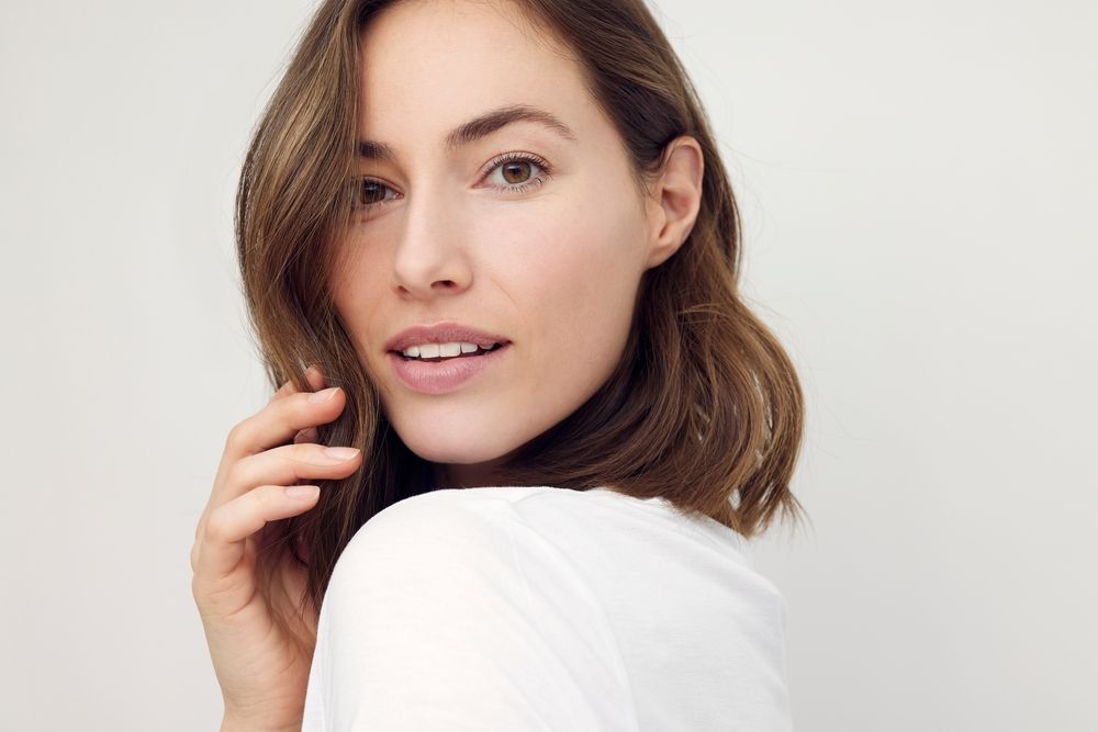 A woman in a white shirt is looking over her shoulder at the camera.