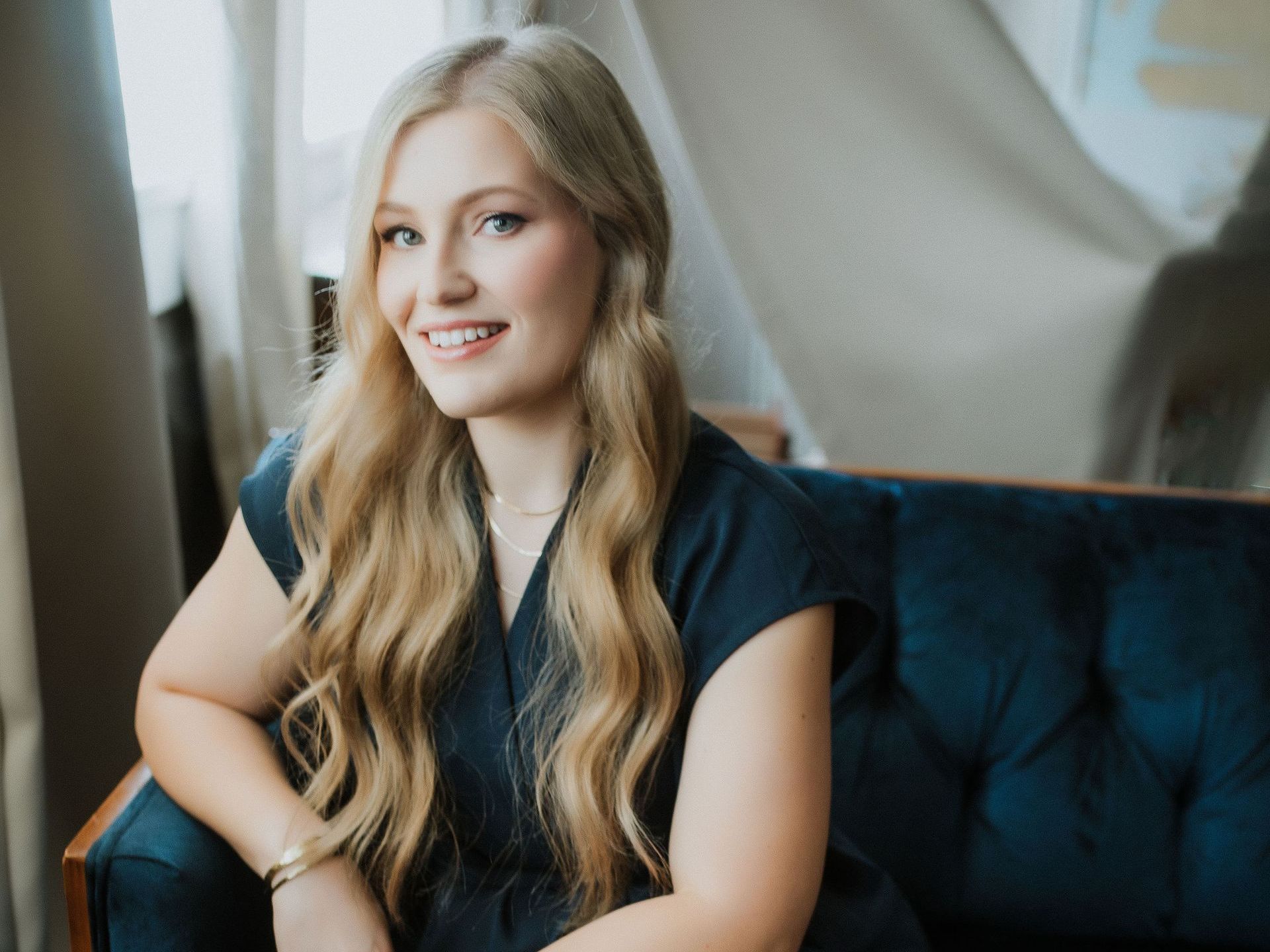 A woman is sitting on a blue couch in front of a window.