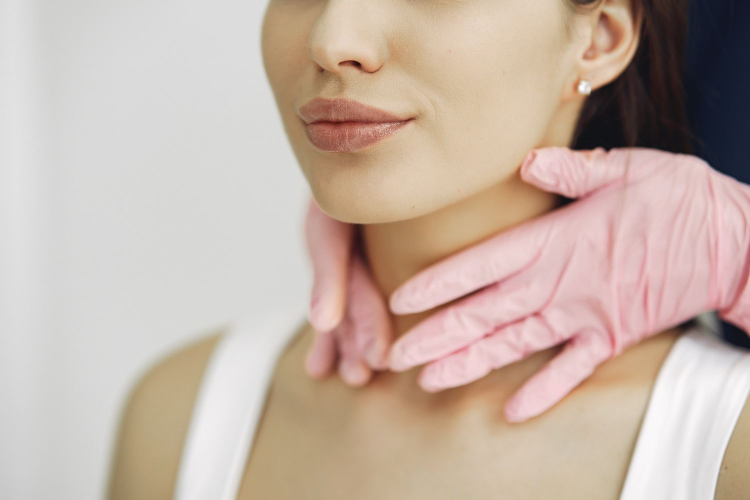 A woman is getting her neck examined by a doctor wearing pink gloves.