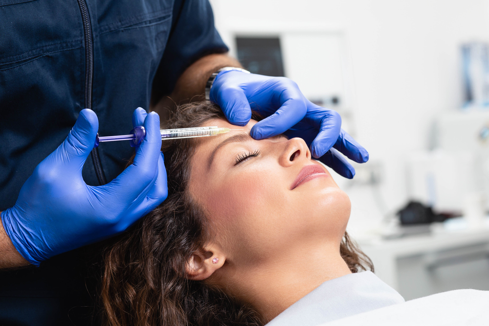 A woman is getting a botox injection in her forehead.