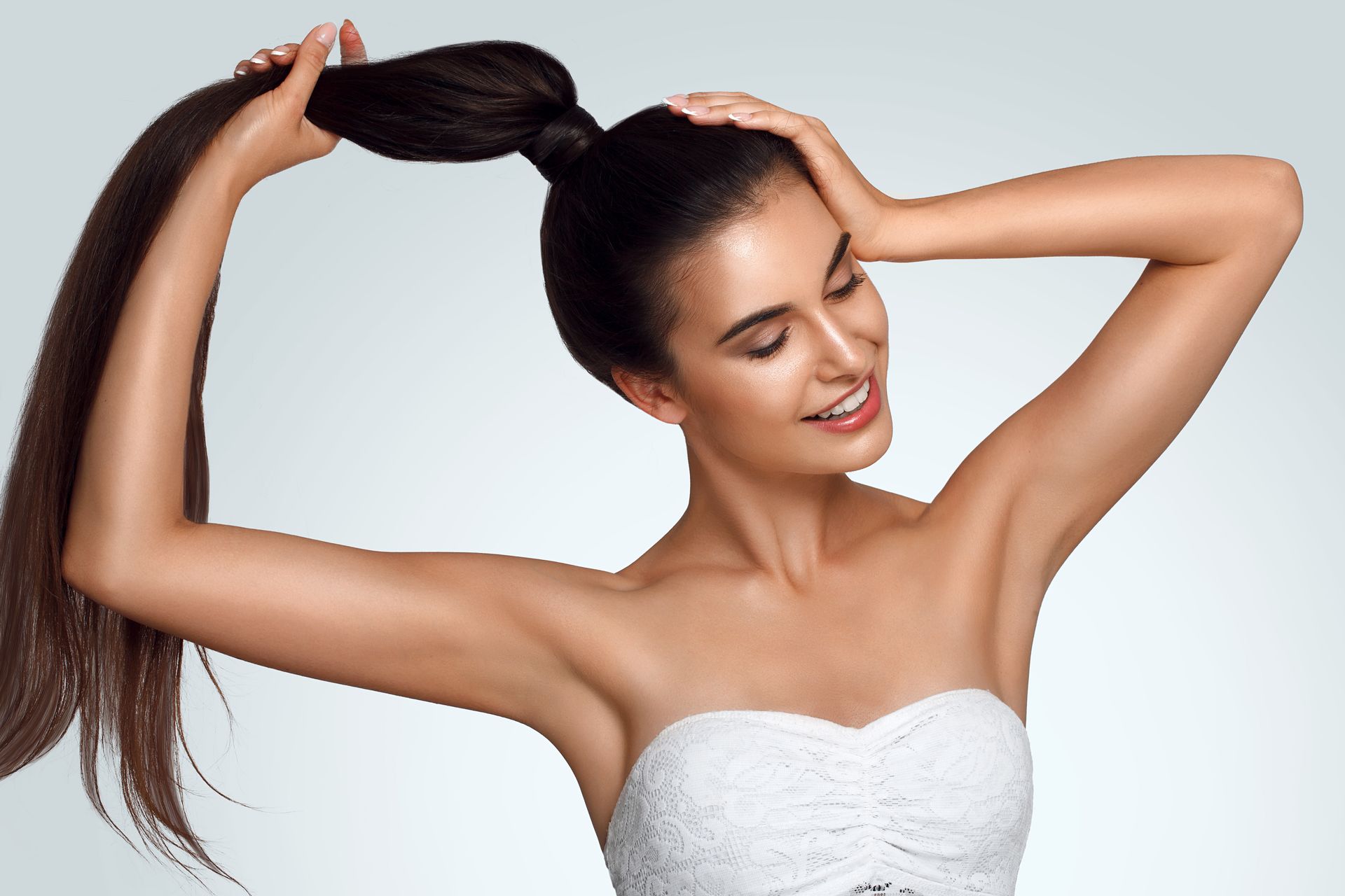 A woman in a white dress is holding her hair in a ponytail.
