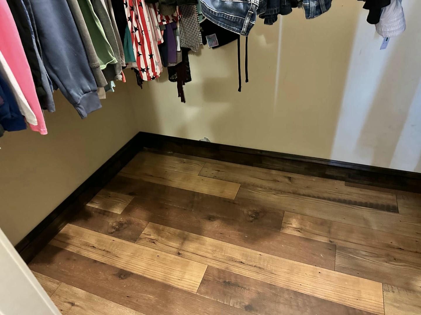 A walk in closet with wooden floors and clothes hanging on the wall.
