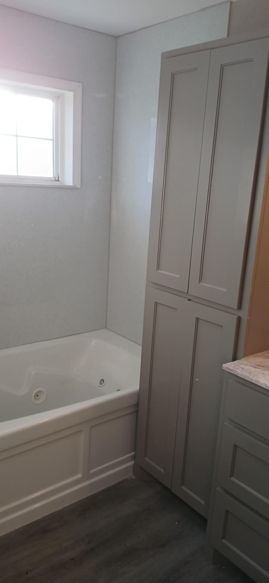 A bathroom with a tub , sink , cabinets and a window.