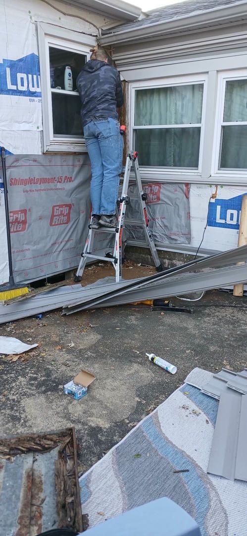 A man is standing on a ladder fixing a window on the side of a house.
