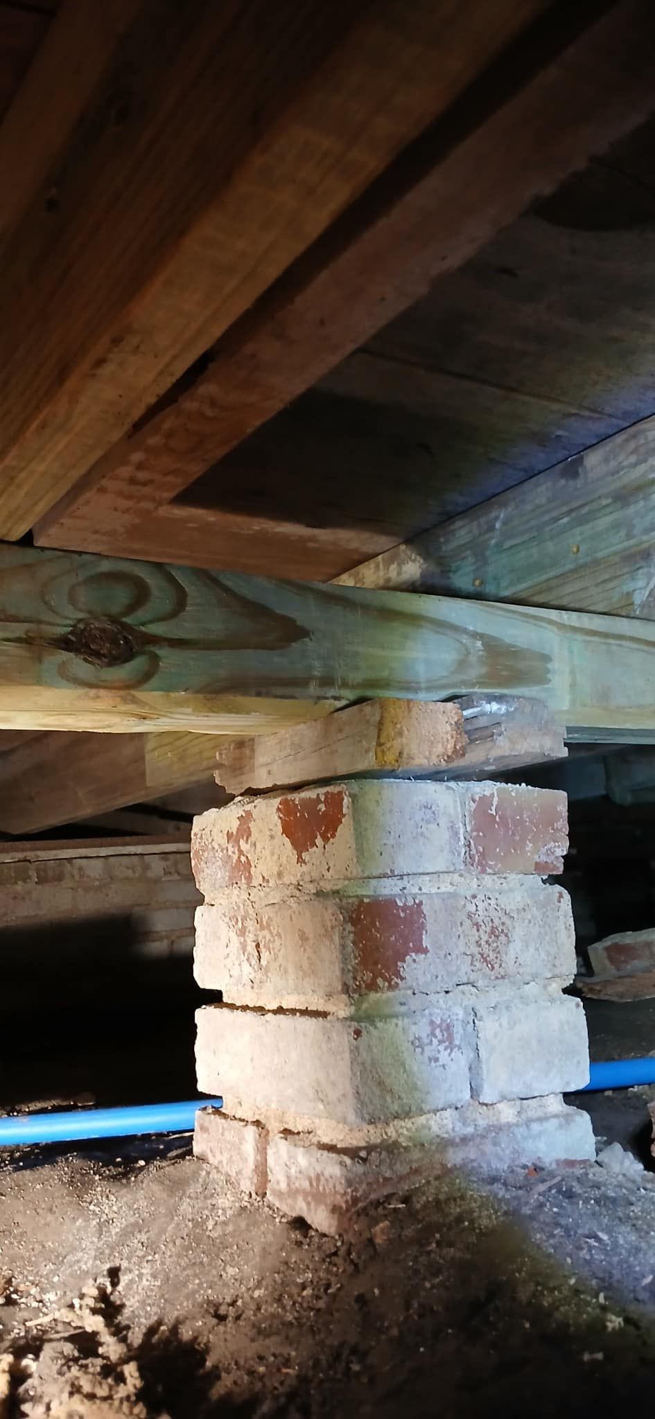 A wooden beam is sitting under a brick wall in a basement.