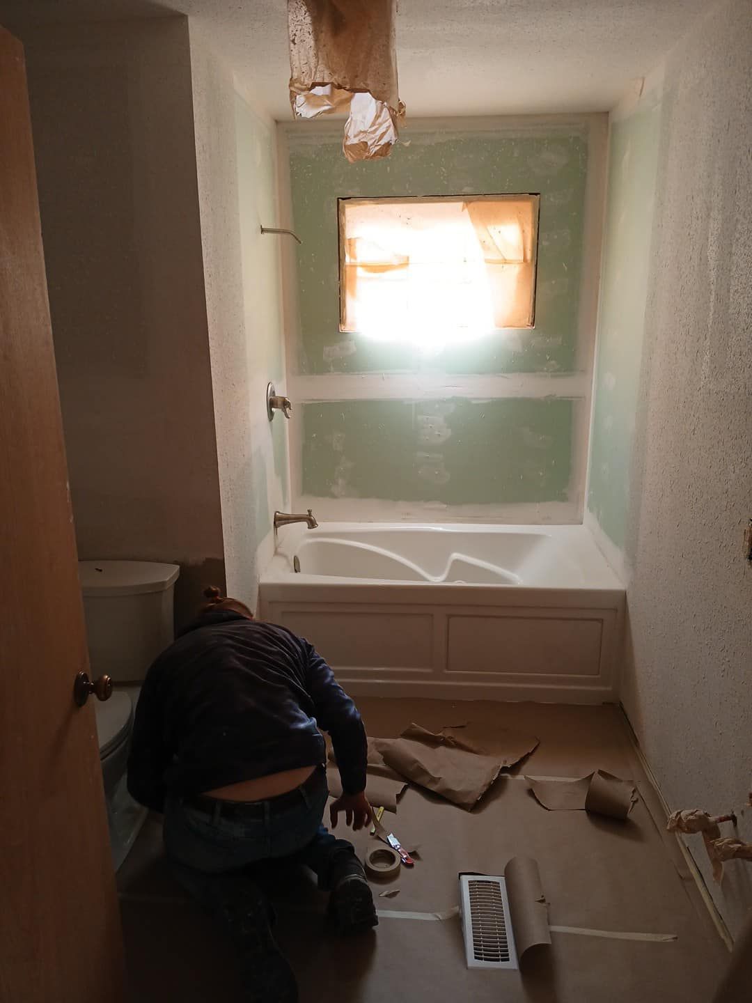 A man is kneeling in a bathroom next to a bathtub.