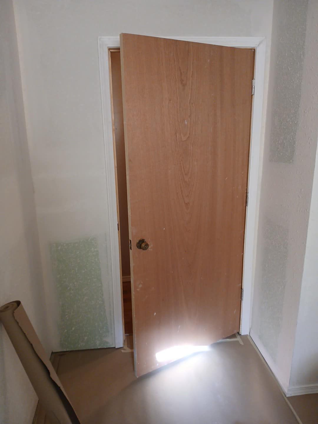 A wooden door is open in a room with a light coming through it.