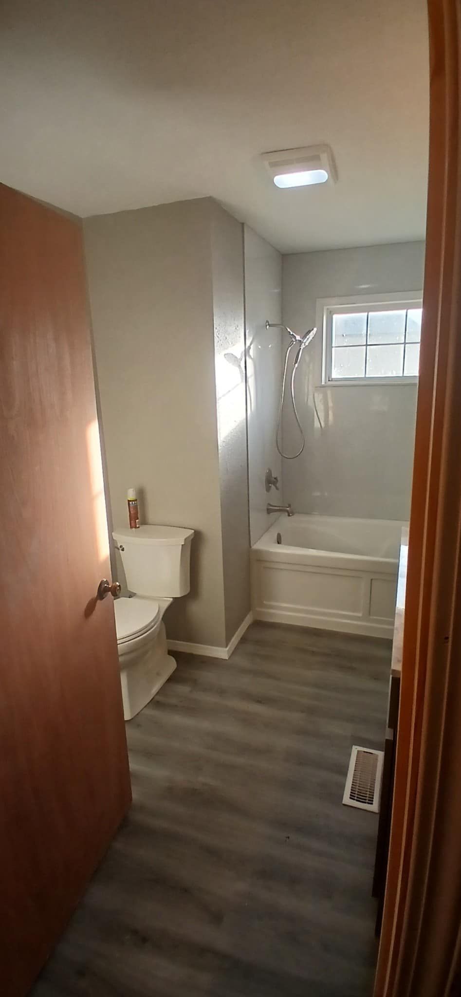 A bathroom with a toilet , tub , shower and window.