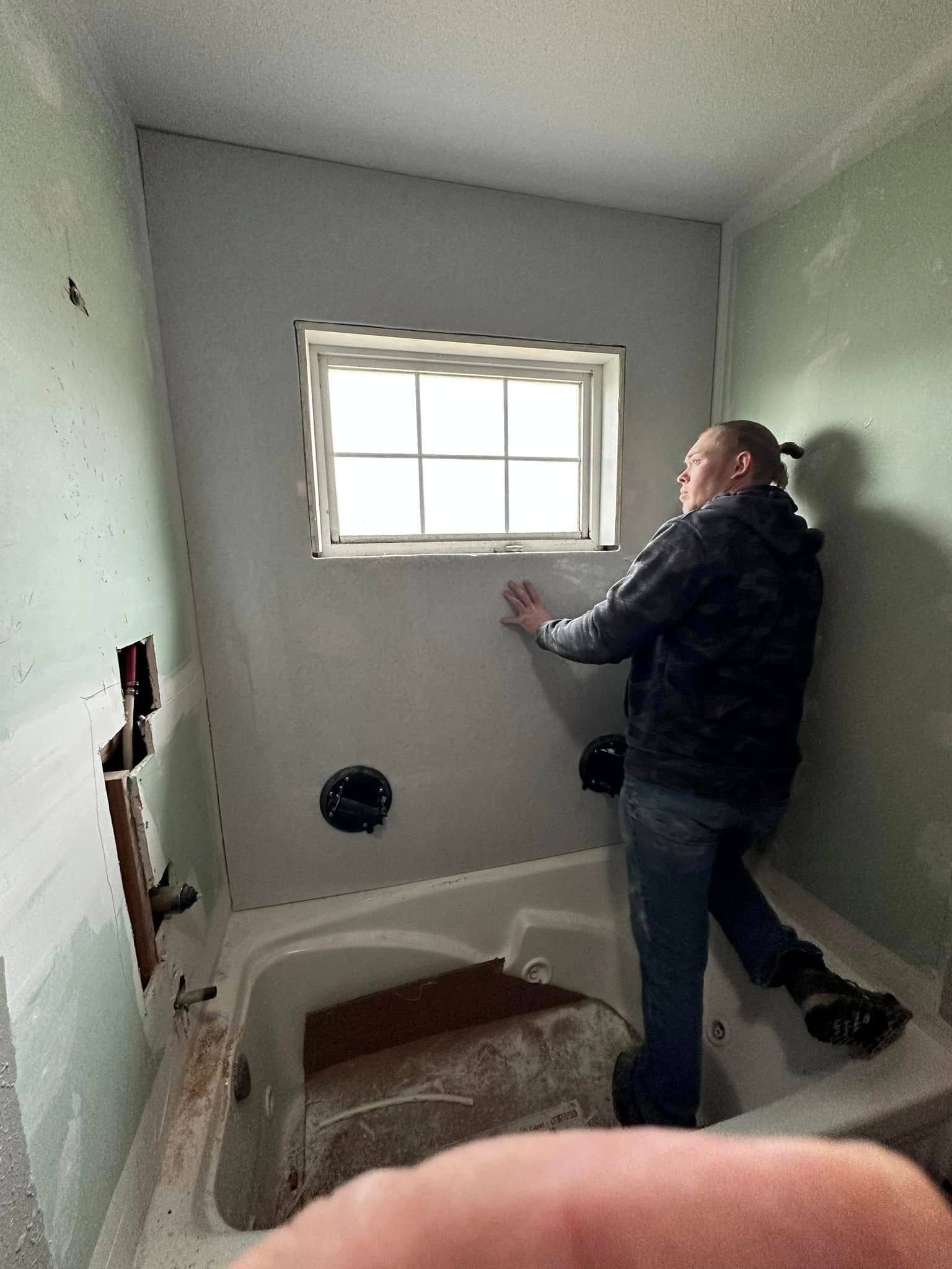 A man is standing in a bathroom next to a window.