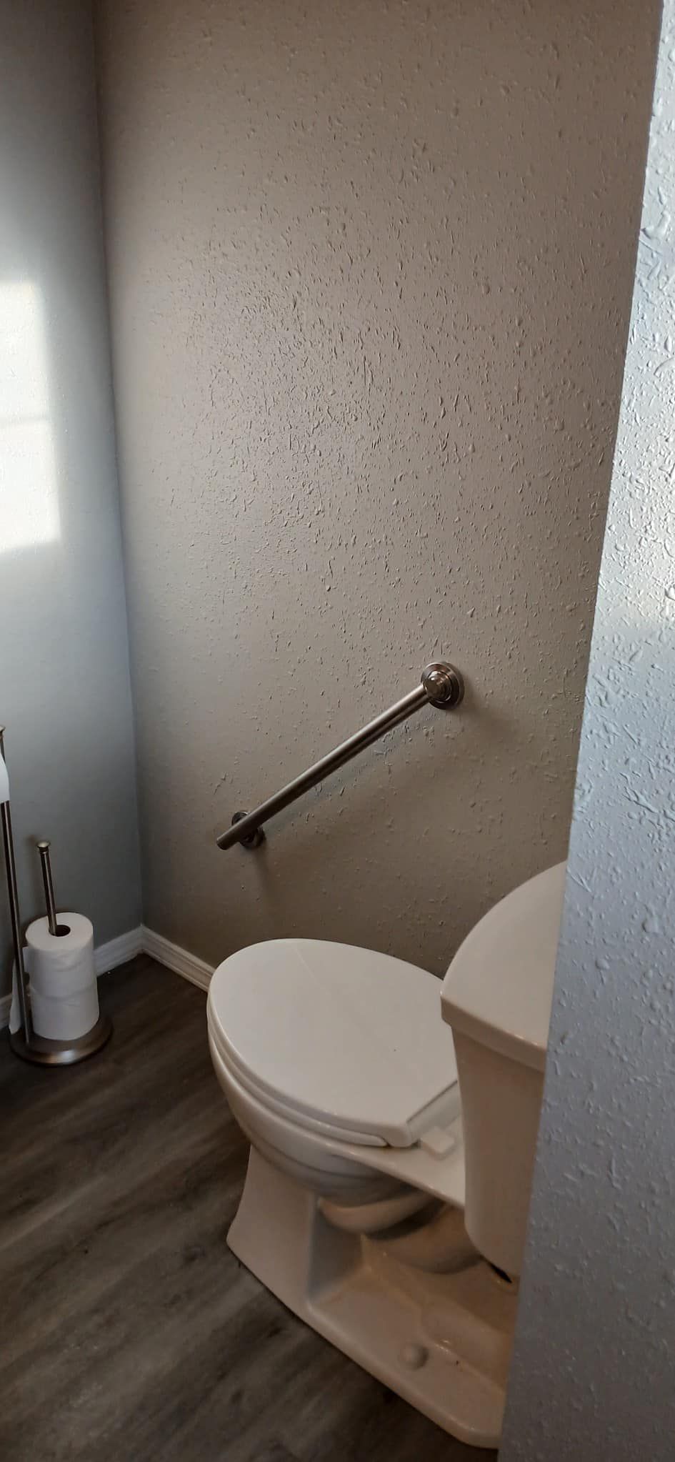 A bathroom with a toilet and a hand rail.