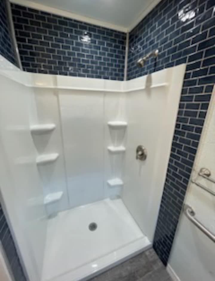 A bathroom with blue brick walls and a white shower stall.