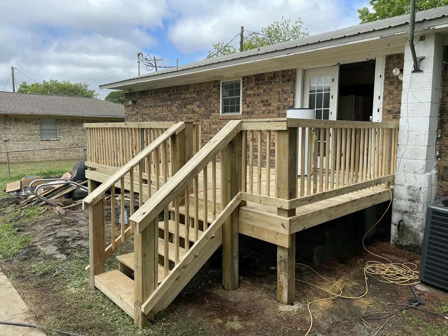 A wooden deck with stairs is in front of a brick house.