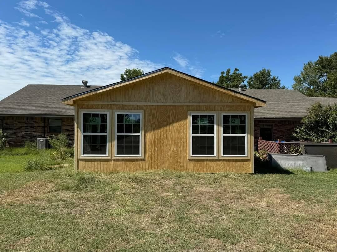 A small house with a lot of windows is sitting in the middle of a grassy field.