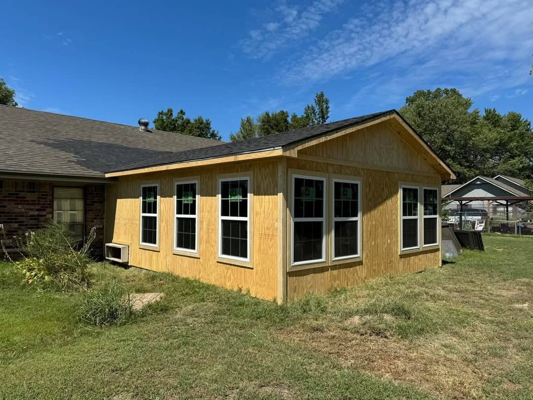 A small house with a lot of windows is sitting in the middle of a grassy field.