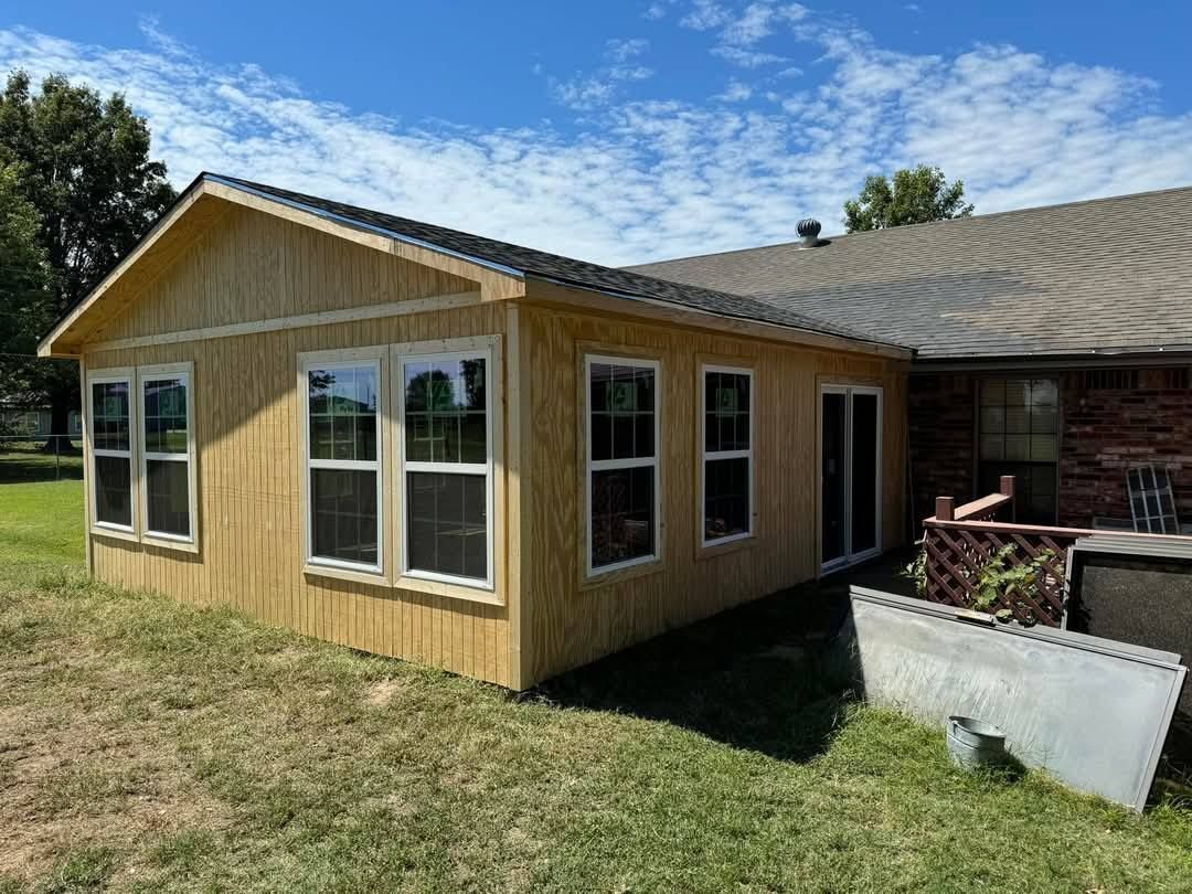A small wooden house with a lot of windows is in the backyard of a house.