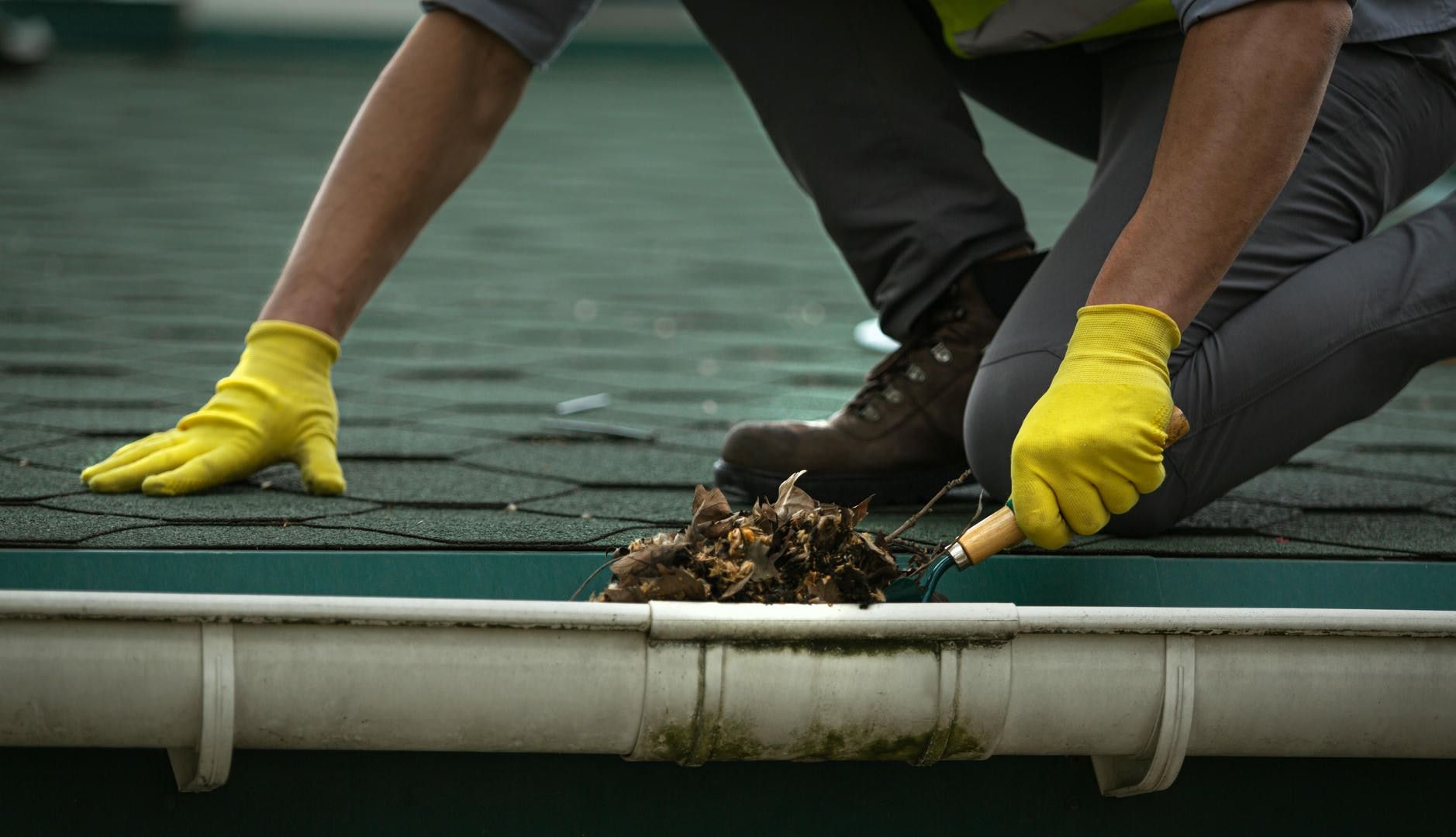 A man wearing yellow gloves is cleaning a gutter on a roof.