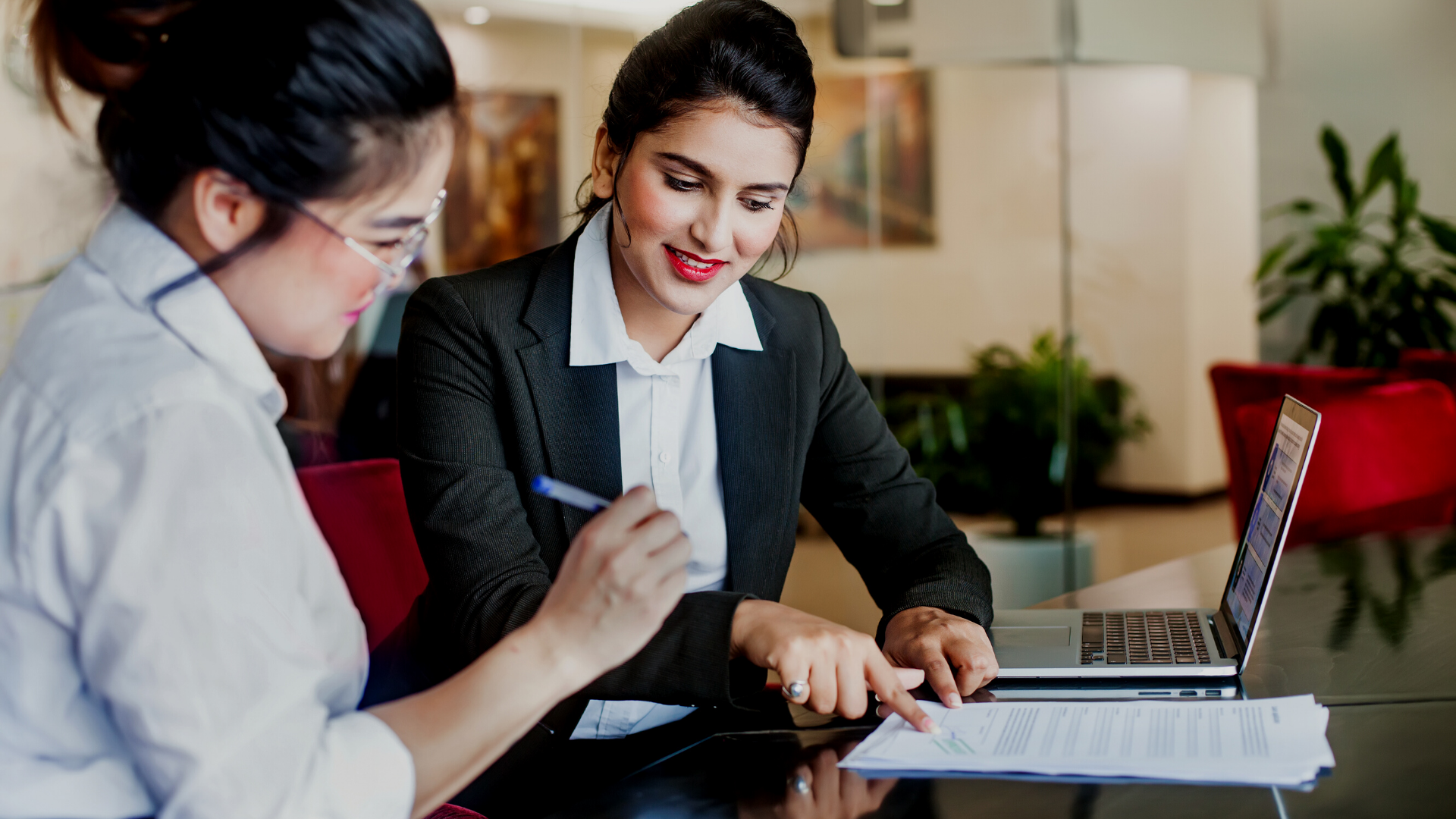 Two women are sitting at a table looking at a laptop computer.