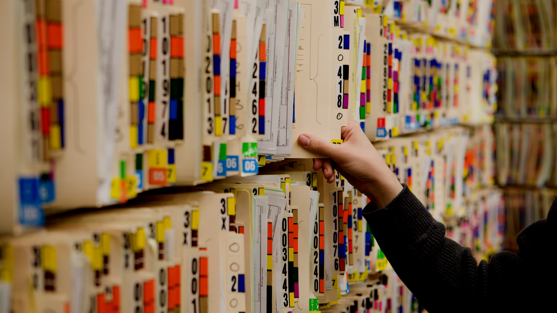 A person is picking up a file from a shelf of medical records.