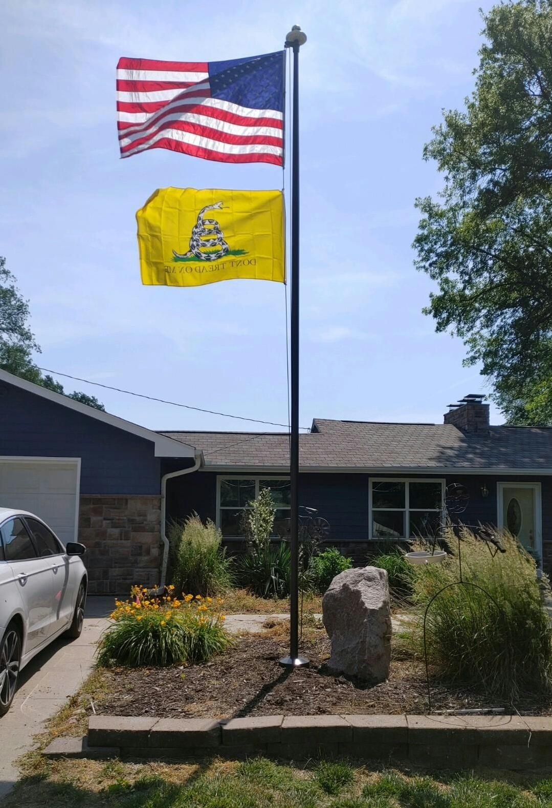 Two flags are flying on a pole in front of a house.