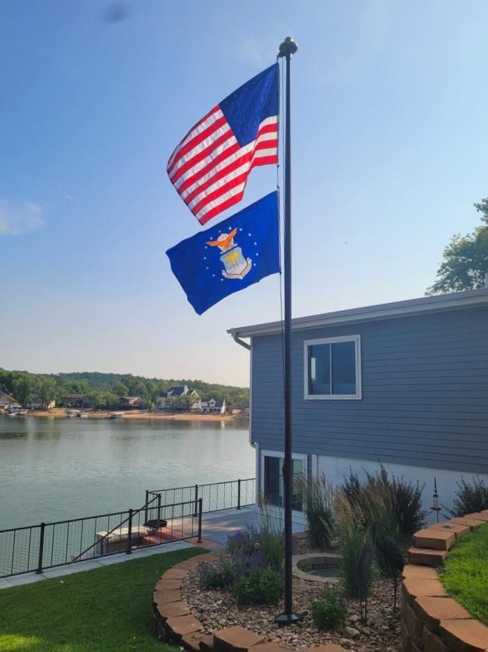 Two flags are flying in front of a house with a lake in the background