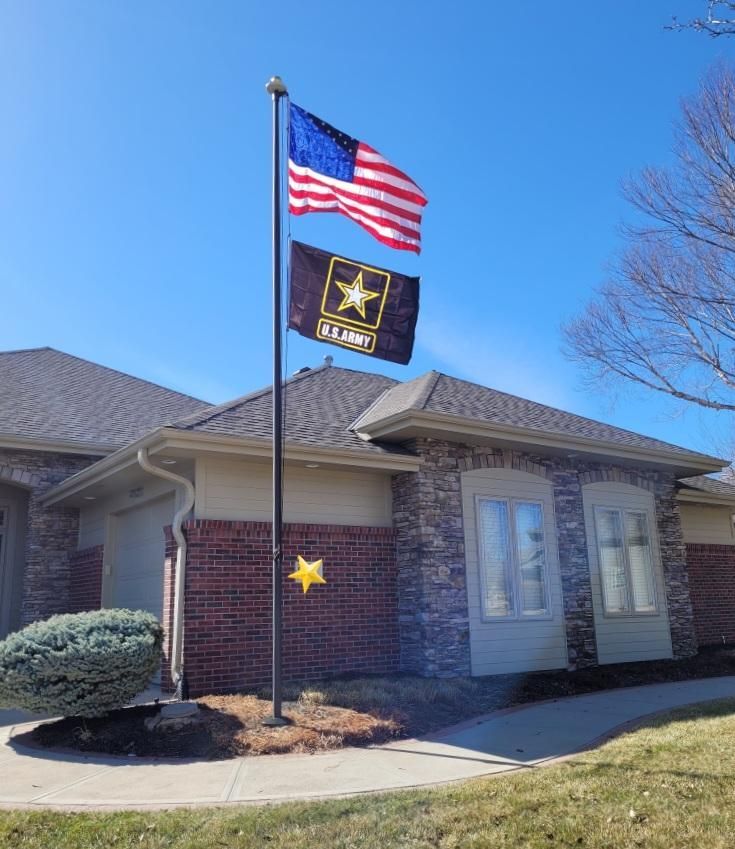 Two flags are flying in front of a brick house.