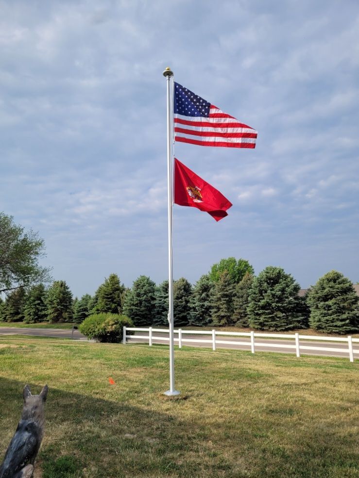 Two flags are flying in a yard with a white fence