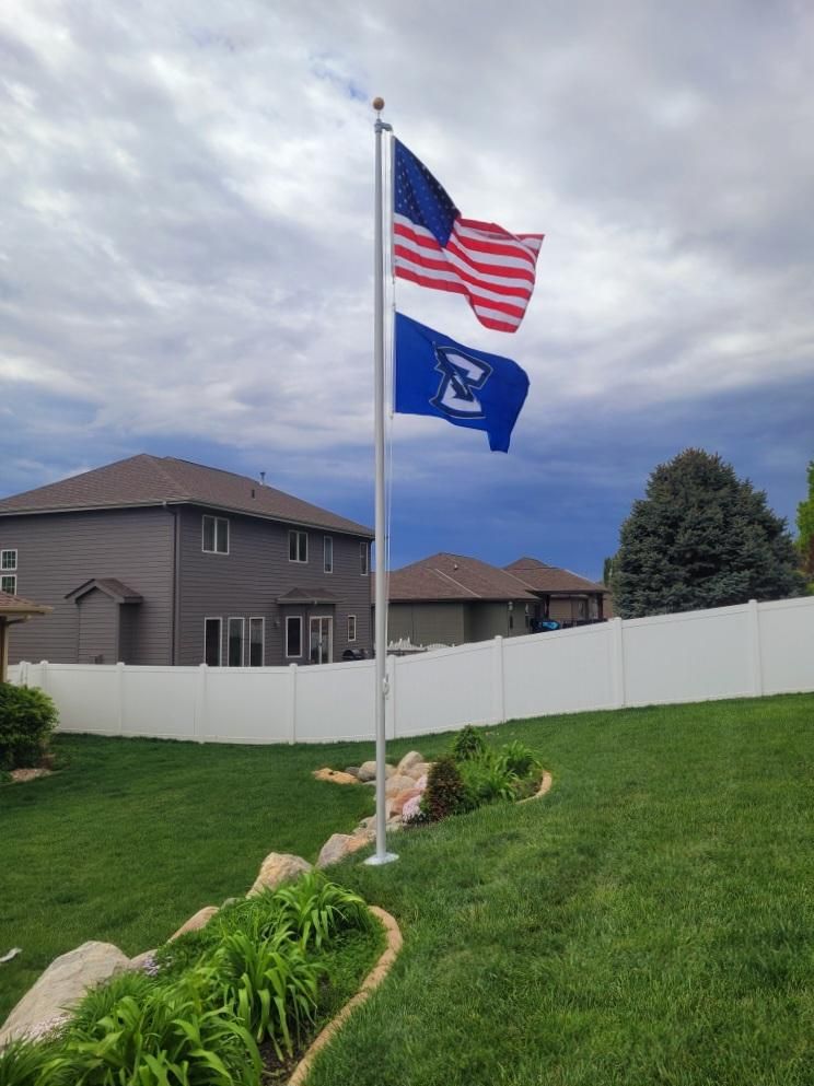 Two flags are flying in a yard with a white fence