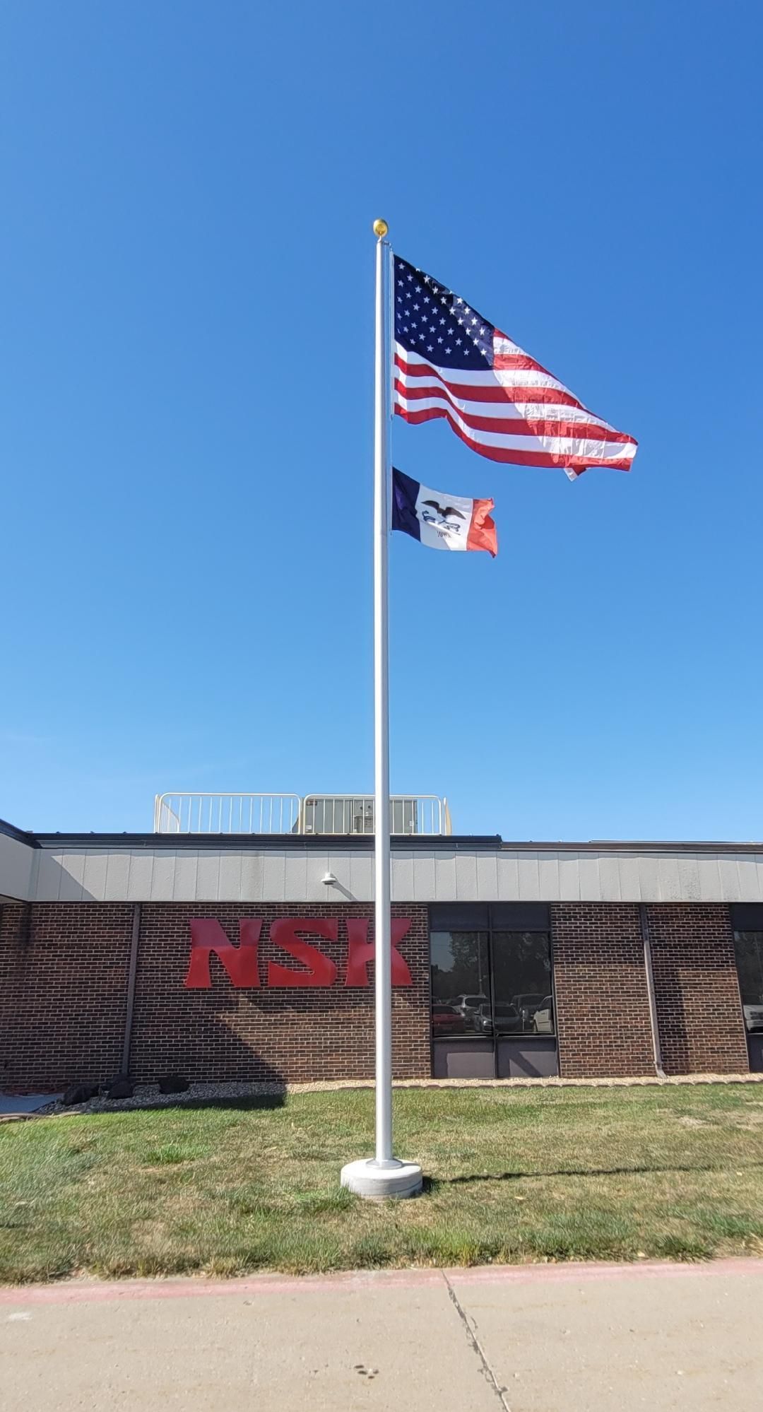 Two flags are flying on a flag pole in front of a building.