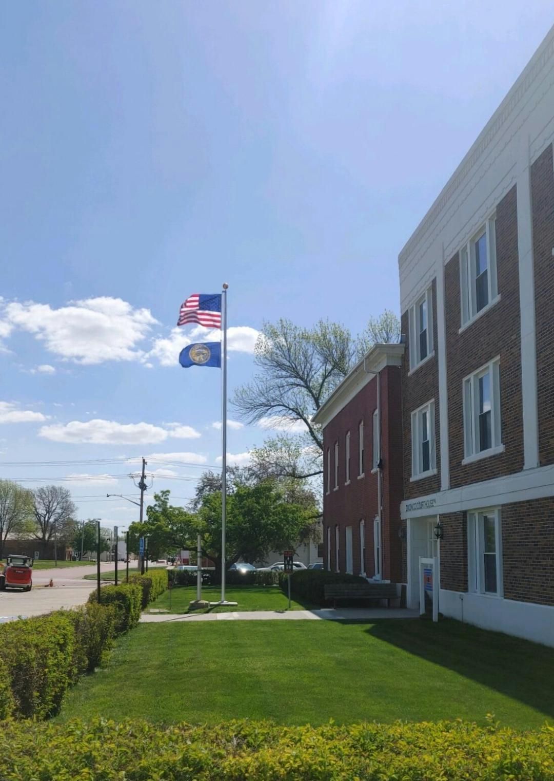 Three flags are flying in front of a brick building