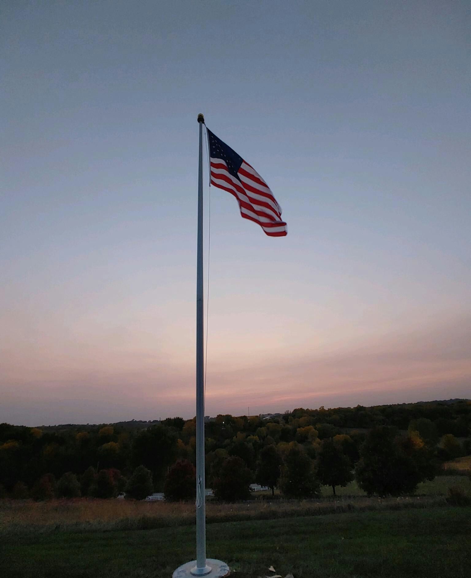 An american flag is flying in the wind at sunset