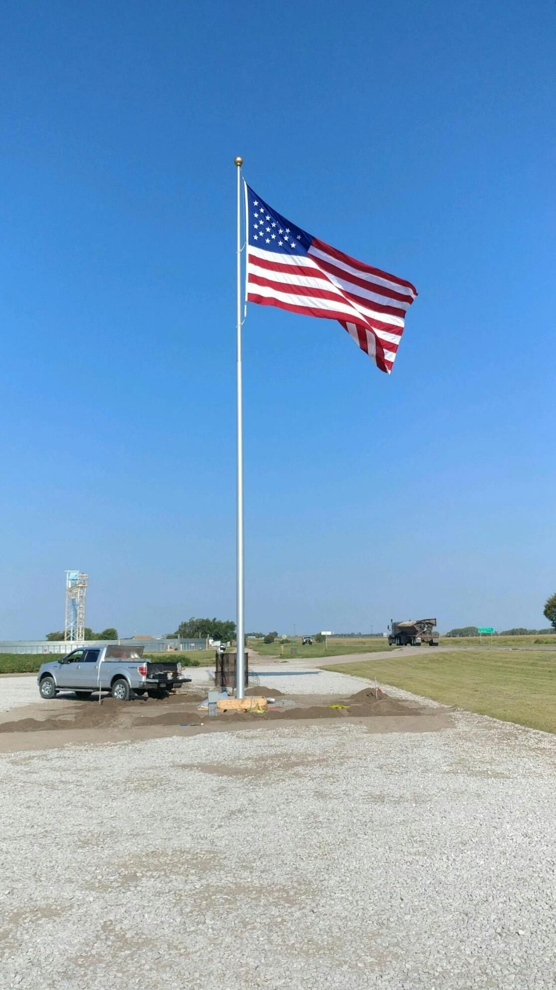 A large american flag is flying in the wind in a parking lot.