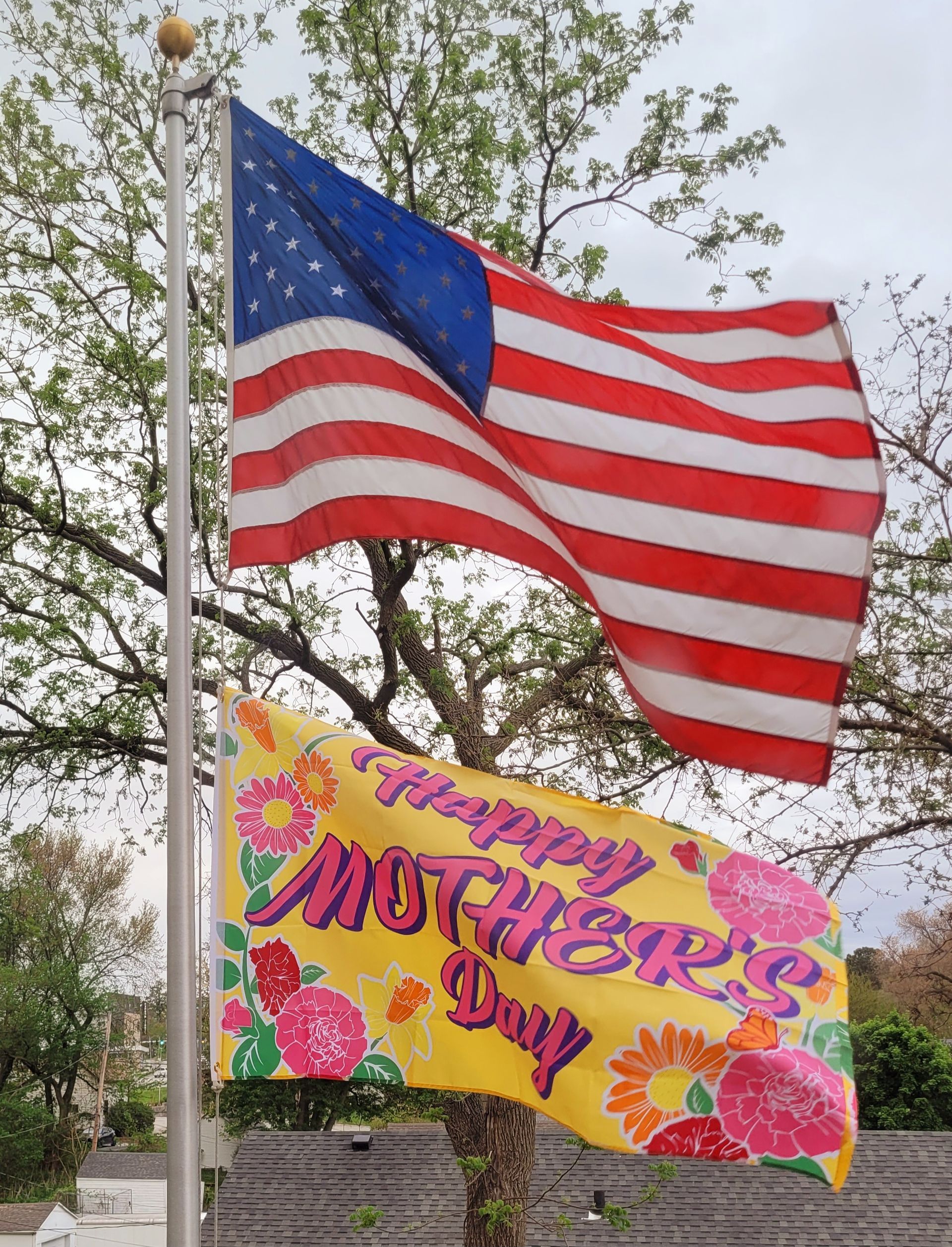 An american flag is flying next to a yellow sign that says happy mother 's day