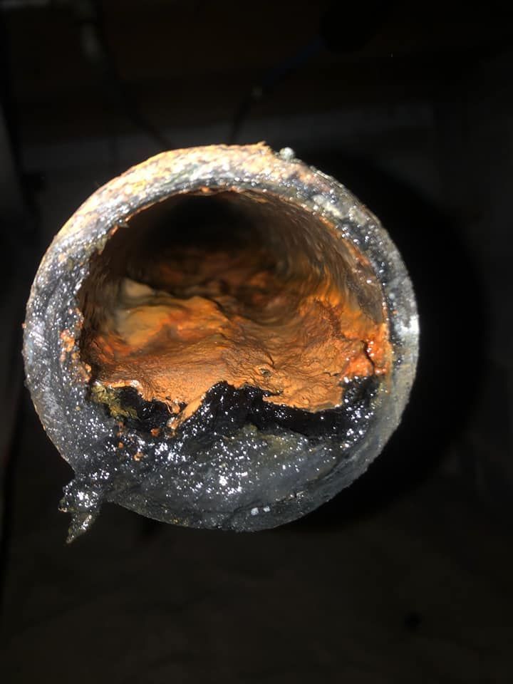 Cross-section of a corroded pipe, showing rust-colored deposits and dark, tar-like residue.