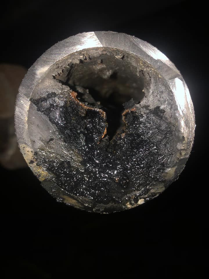 Cross-section of a corroded metal pipe. The inside is filled with dark, flaky buildup; the outer is shiny metal.