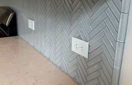 Herringbone patterned gray tile backsplash above a light countertop, with white electrical outlets.