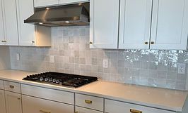 Kitchen with white cabinets, stainless steel range hood, gas cooktop, and light-colored backsplash.