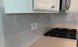 Kitchen with light gray subway tile backsplash, white cabinets, and a black stovetop.