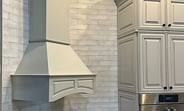 Gray kitchen range hood and cabinets on white brick wall.