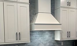 White kitchen cabinets with black handles and a matching range hood over a blue tiled backsplash.