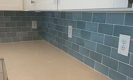 Kitchen backsplash with blue subway tiles and light-colored countertop. Includes electrical outlets.