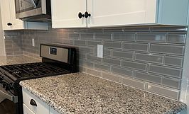 Kitchen with granite countertop, gray subway tile backsplash, and white cabinets. Stainless steel appliances.