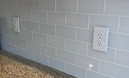 Light gray subway tile backsplash with two white electrical outlets.