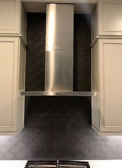 Stainless steel range hood with black tile backsplash, flanked by cream cabinets.