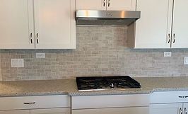 Kitchen with white cabinets, light gray backsplash, stainless steel range hood, and black cooktop.