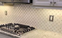 Kitchen with tiled backsplash, stove, and countertops; warm lighting and white cabinets.