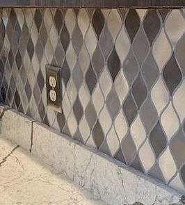 Backsplash with gray, white, and dark gray diamond-shaped tiles above a countertop with a marble-like edge.