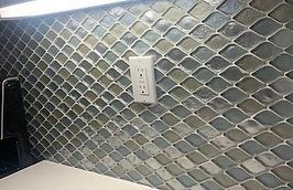 Diamond-shaped mosaic tile backsplash with a white electrical outlet. Blue, green, and gray tiles cover the wall.