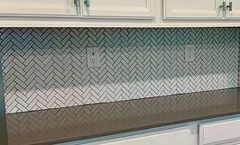Herringbone tile backsplash above a dark countertop and white cabinets.