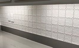 White, patterned tile backsplash above a light-colored countertop. Recessed lighting illuminates the wall.